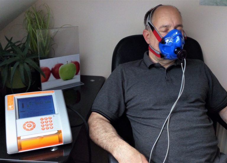 Mann mit Atemmaske sitzt neben einem gesundheitlichen Gerät und Pflanzen.