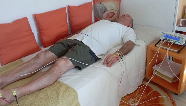 Mann liegt entspannt auf einem Bett mit Elektroden an Armen und Beinen.